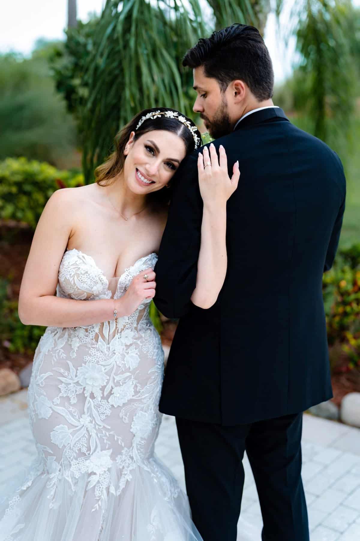 Bride holding her groom's arm and smiling at the camera