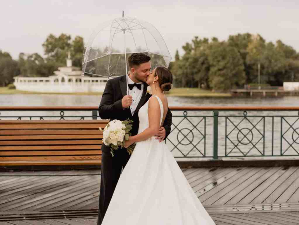 Bride and groom kissing beneath a clear umbrella