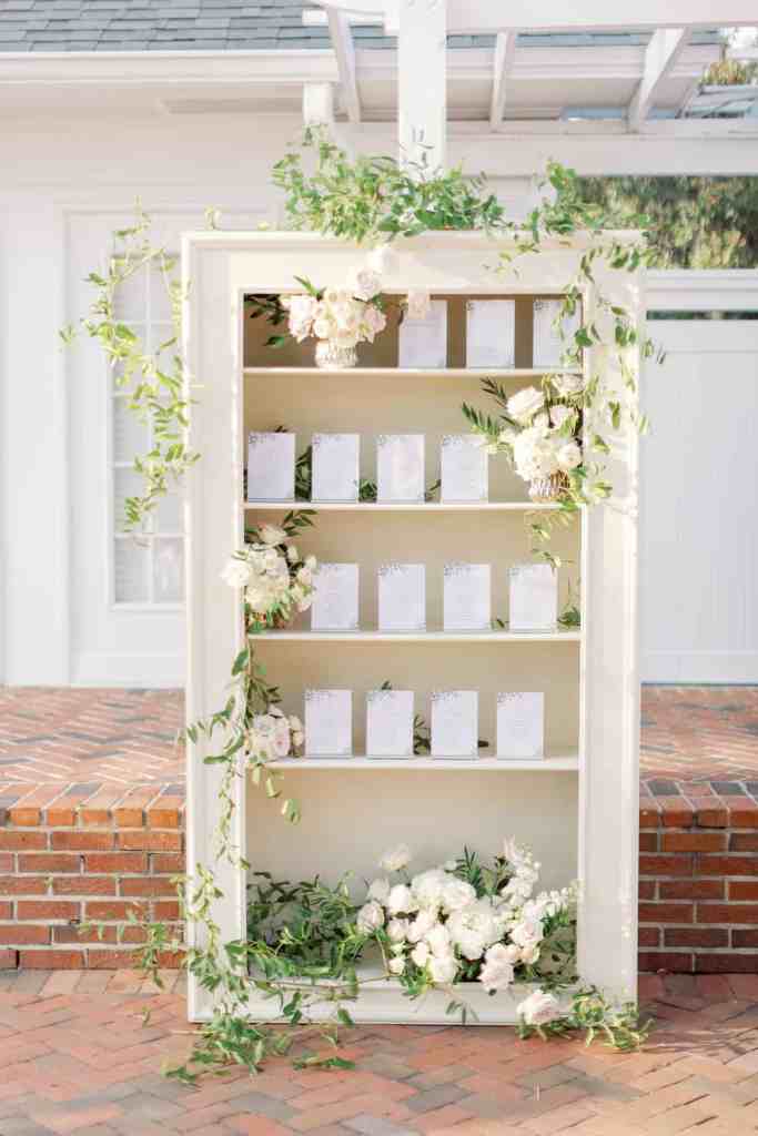 Floral-decorated bookcase with table assignments on it for a tent reception