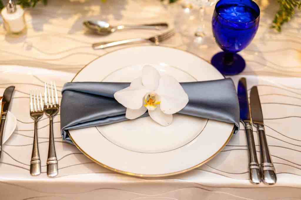 Wedding reception plate with a dusty blue napkin topped with a single white orchid