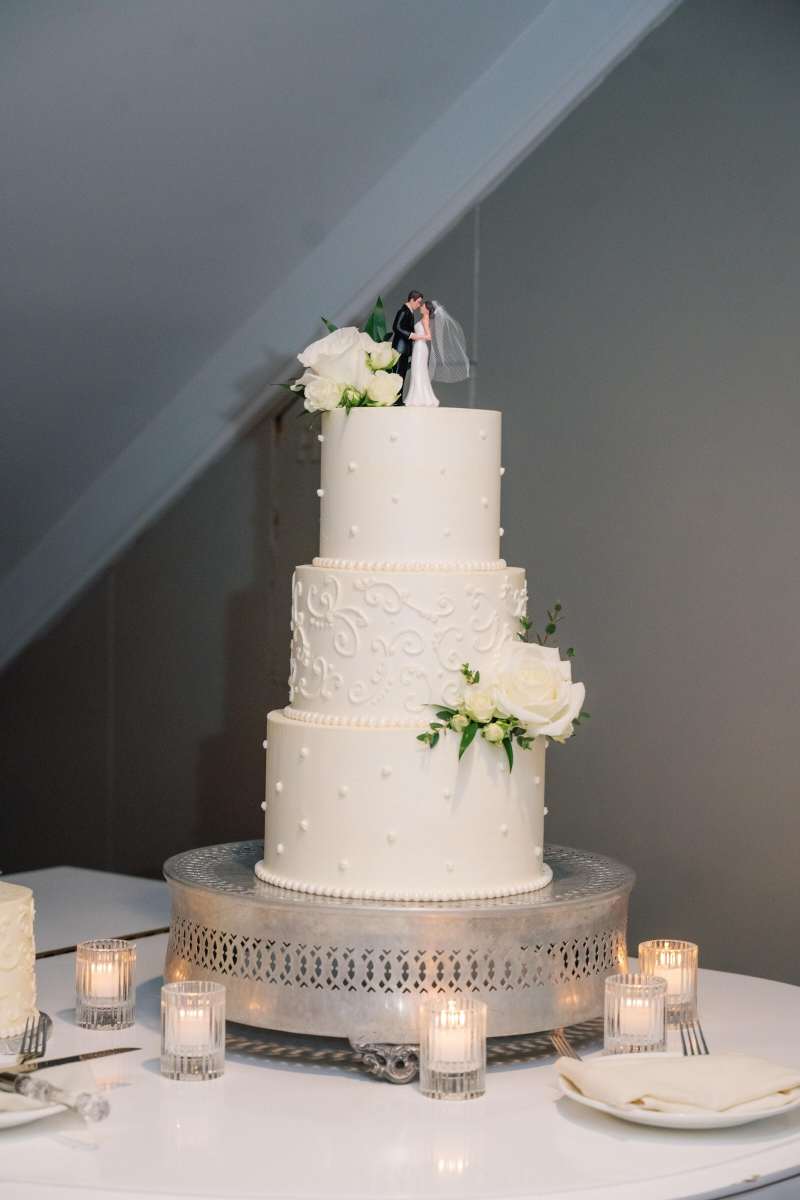 Three tiered wedding cake decorated in white floral and greenery