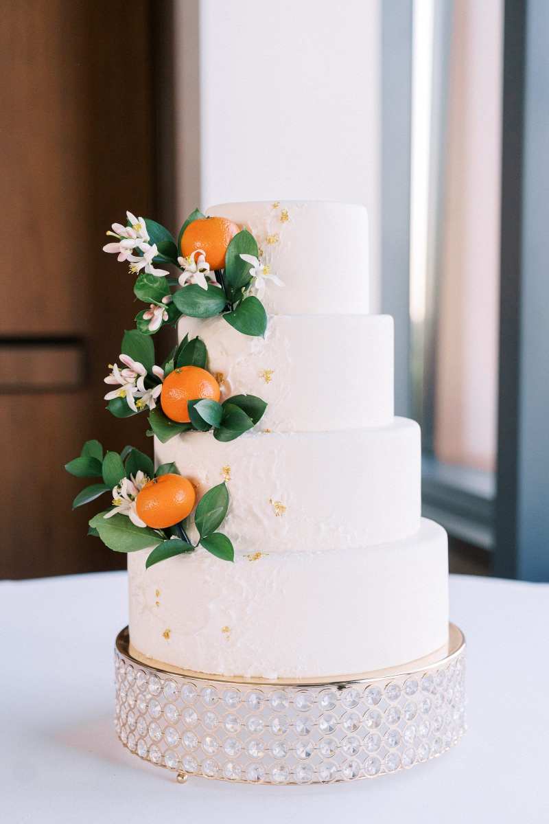 Four tiered white wedding cake decorated with tangerines and greenery