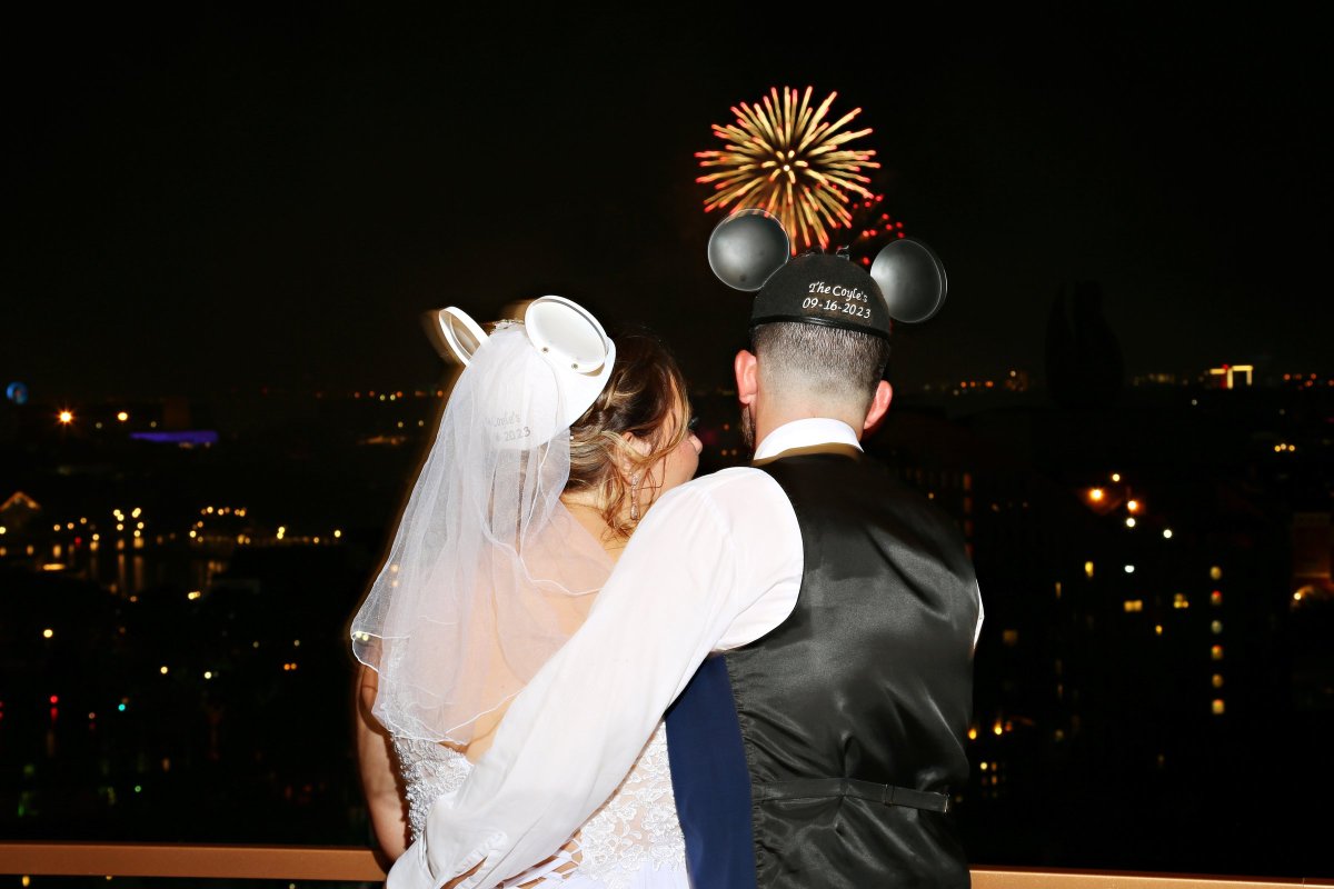 Bride and groom wearing Mickey and Minnie ears and watching fireworks