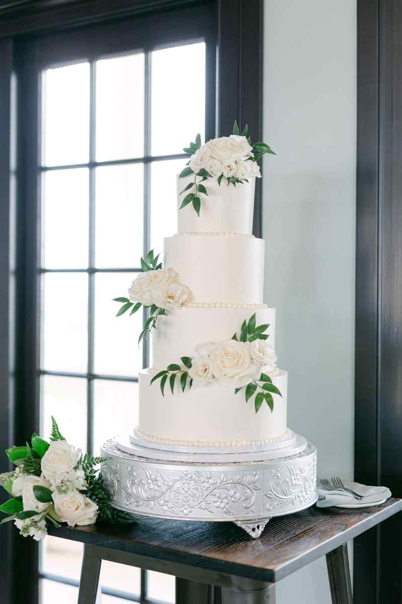 Four-tiered white wedding cake decorated with white floral and greenery