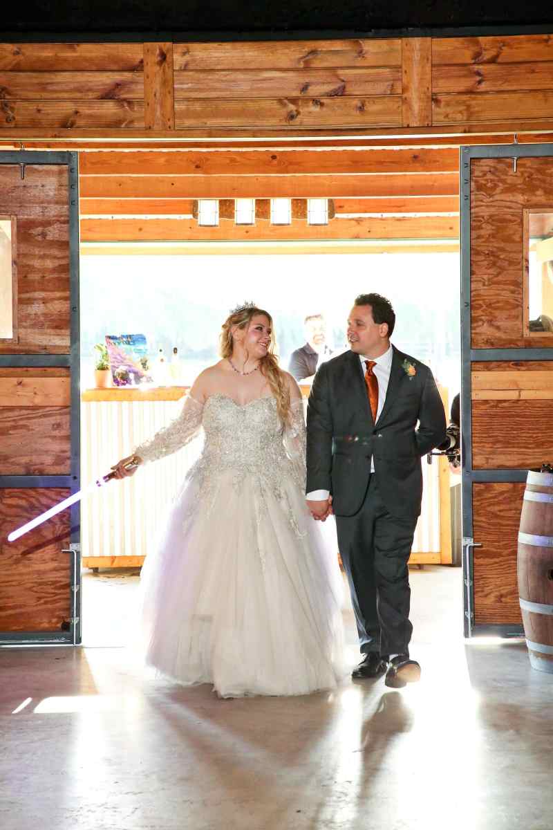 Bride and groom entering their reception holding lightsabers