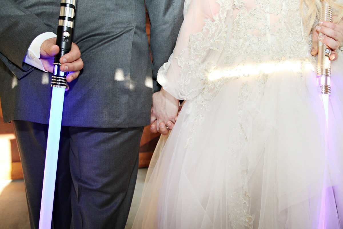 Bride and groom holding lightsabers behind their backs