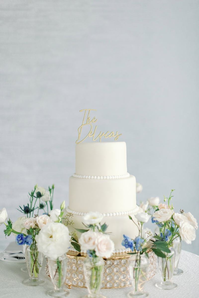 Two tiered white wedding cake surrounded by white and pale blue flowers