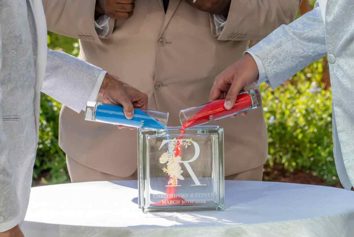Grooms pouring blue and red sand into a sand ceremony vessel