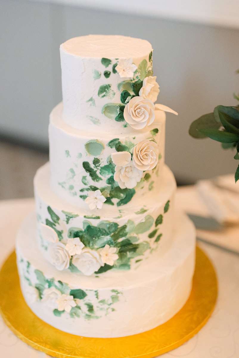 Four tiered wedding cake decorated with white floral and greenery details