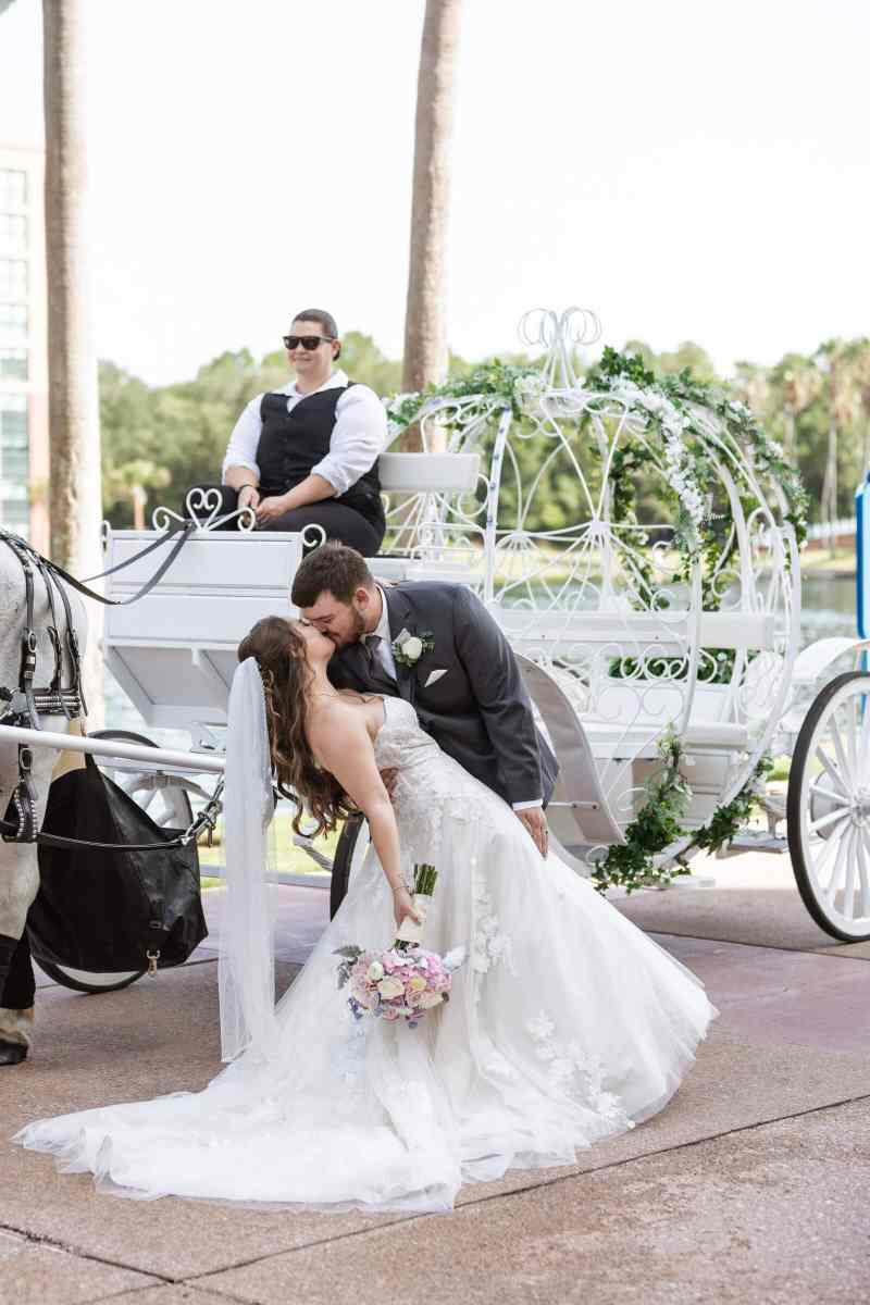 Groom dipping his bride and kissing her in front of a horse and carriage